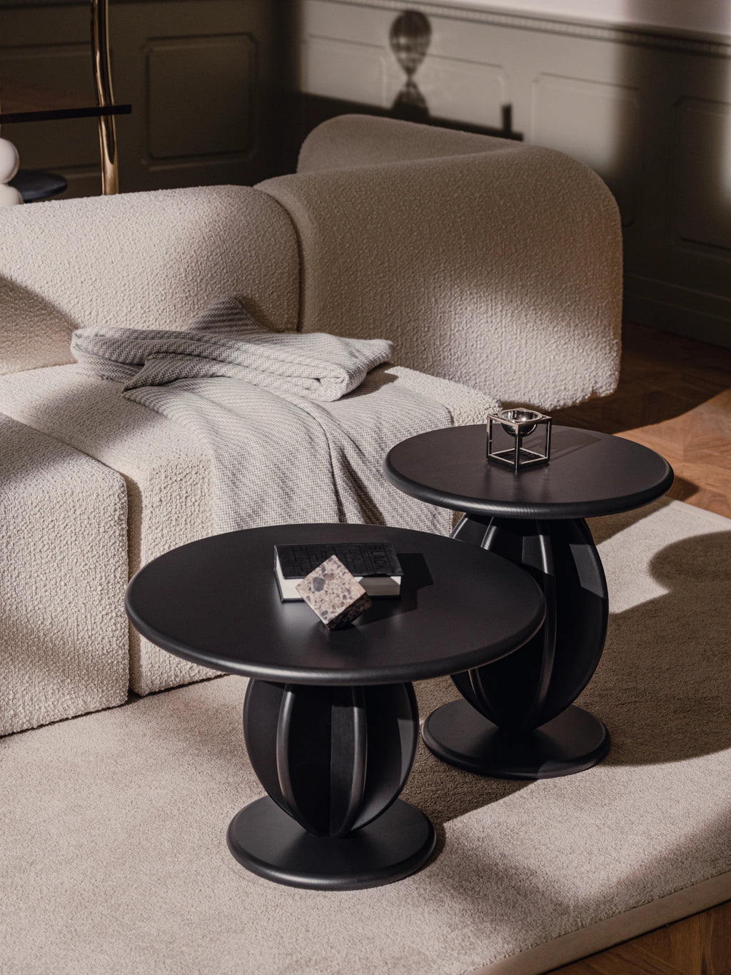 TAMO Citrus Coffee Table set with two matte black wooden tables featuring sculptural, fluted cylindrical bases next to a cream boucle sofa. A luxurious statement for modern living spaces.
