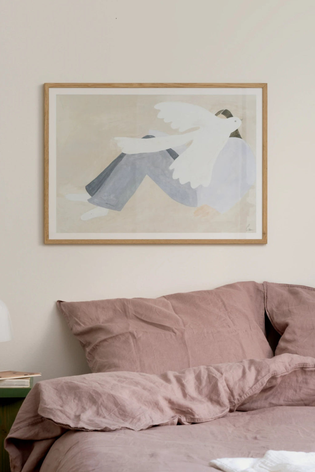 The Poster Club Bright Bird, an abstract art print featuring a minimalist figure in light blue-grey pants and a white top, embracing a large white bird, all set against a soft beige background. This contemporary wall art is framed in a light natural oak frame, perfect for a modern bedroom, minimalist living room, or a Scandinavian gallery wall.