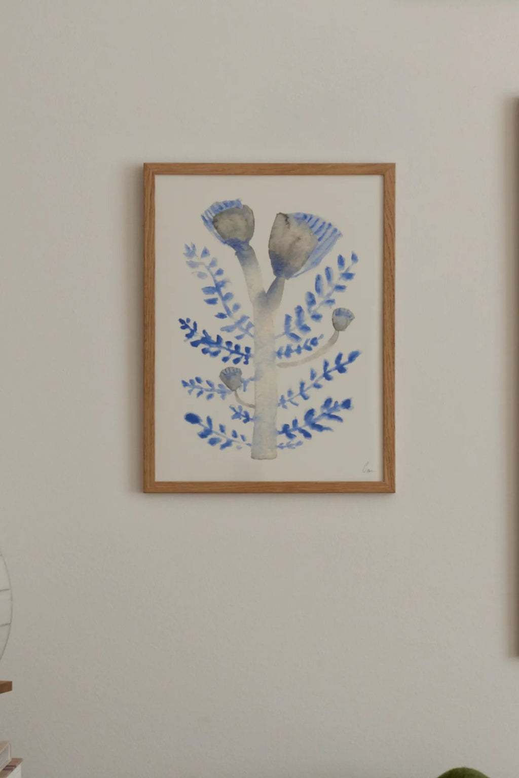 The Poster Club Januari, a charming watercolor botanical art print featuring a stylized tree with soft grey-blue buds and vibrant blue leaves on a crisp white background. This organic modern wall art is beautifully presented in a natural oak frame, highlighting its folk art inspired design and delicate brushstrokes. Ideal for creating a serene atmosphere, this framed art print is perfect for Scandinavian bedrooms, minimalist living rooms, or a curated gallery wall.