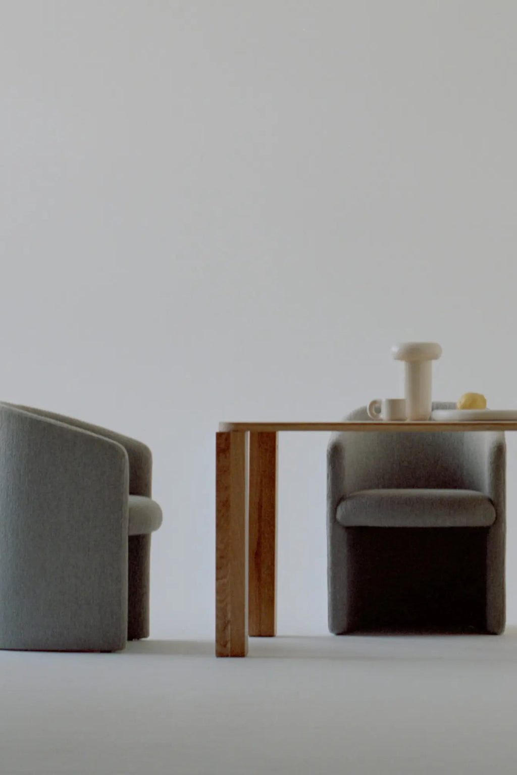 New Works Covent Club Chair in light gray felted upholstery, showcasing its modern rounded back and deep seat beside a light oak table in a studio setting. Perfect for contemporary interiors.