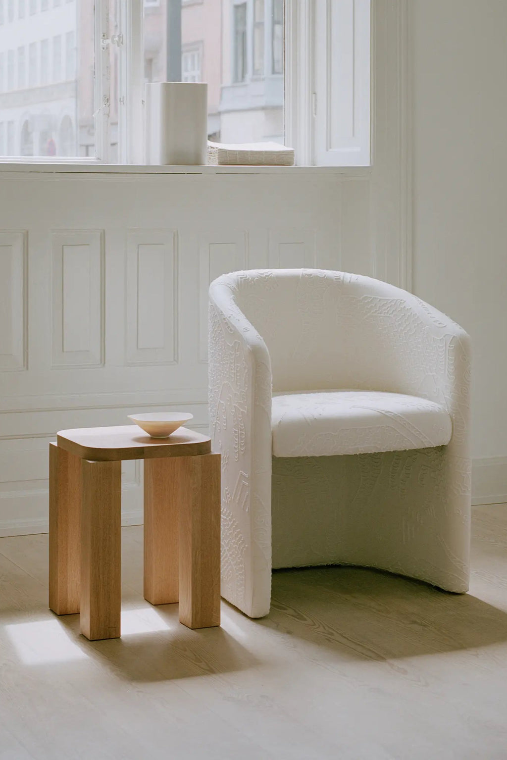New Works Covent Club Chair, a sculptural and inviting contemporary club chair upholstered in a rich, off-white textured fabric with an intricate, subtle jacquard pattern. Its organic, rounded silhouette and deep, comfortable seating make it a perfect minimalist lounge chair or elegant accent piece for modern interiors. Ideal for a cozy reading nook, stylish living room, or refined bedroom.