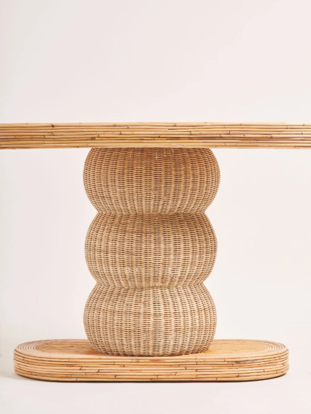 Heaps & Woods Barney Console, an organic modern console table crafted from natural rattan and bamboo, featuring a rectangular top and oval base made from parallel rattan poles, supporting a distinctive central column of three stacked, rounded woven rattan segments in a warm, natural finish. This stylish piece is ideal for coastal-inspired entryways, boho living rooms, or contemporary hallway decor.