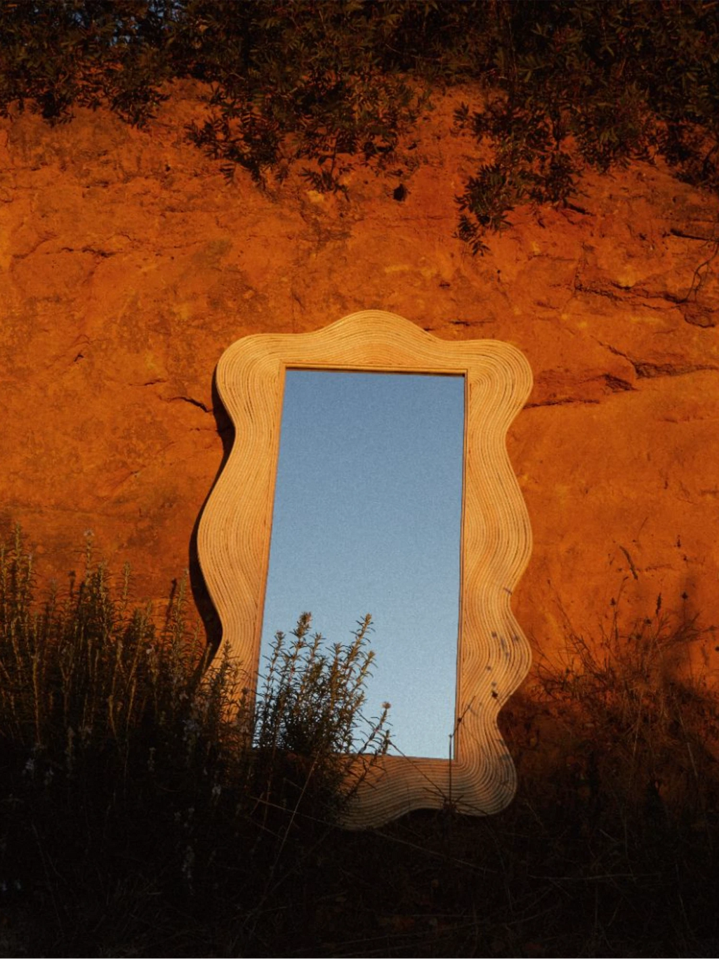Heaps & Woods Sofia Mirror, a distinctive organic modern wall mirror featuring a natural blonde wood frame with a unique layered wavy texture and free-form edges. This sculptural decorative mirror reflects the sky, offering a contemporary bohemian accent for stylish living rooms, bedrooms, or entryways.