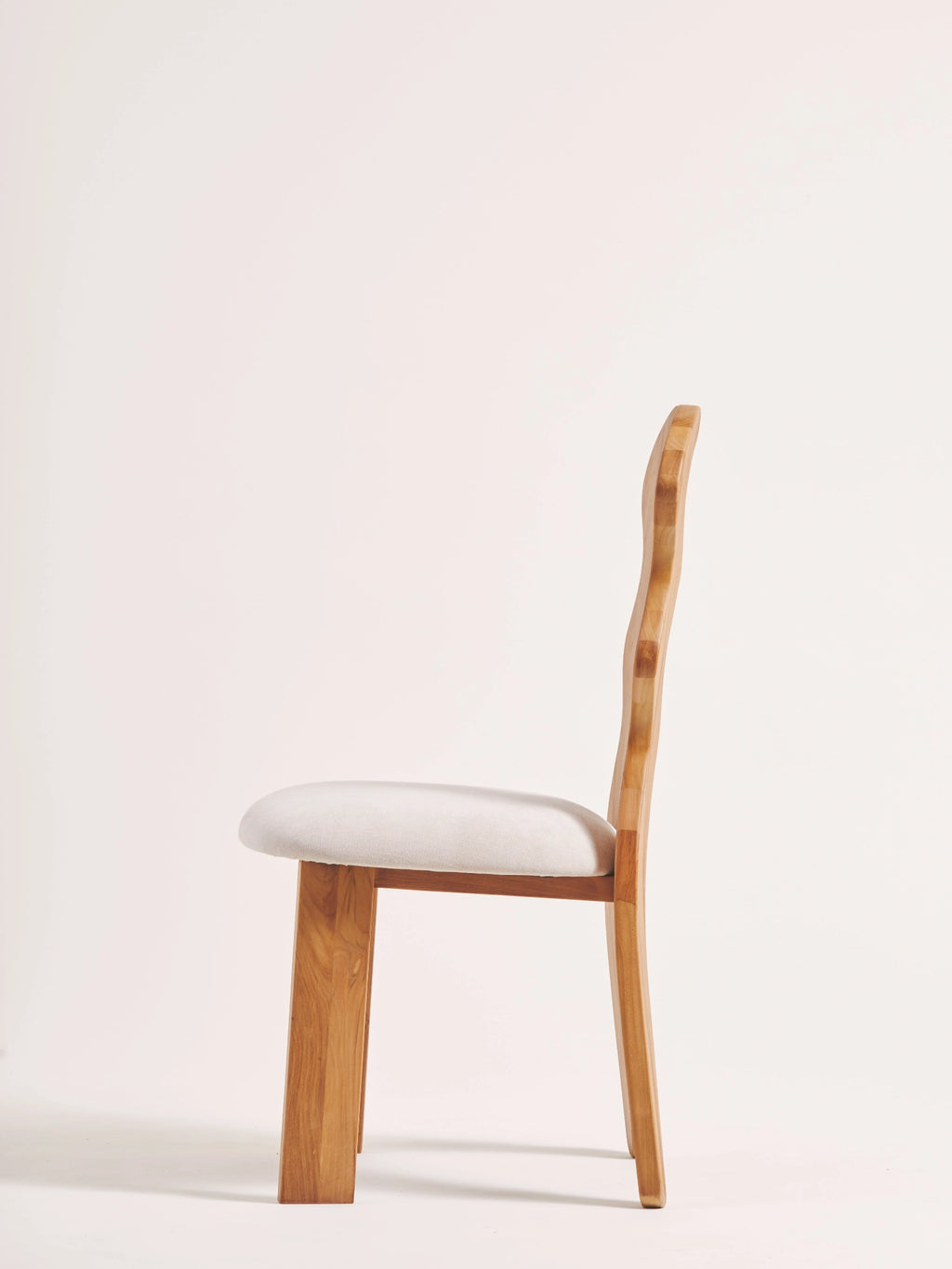 Heaps & Woods Curvy Dining Chair, an organic modern dining chair crafted from light solid wood with a distinctive wavy, sculptural backrest and a comfortable cream fabric upholstered seat. Its minimalist design features thick rectangular front legs and rounded back legs, creating a contemporary silhouette. Ideal as a stylish light wood dining chair for modern dining rooms or sophisticated kitchen spaces.