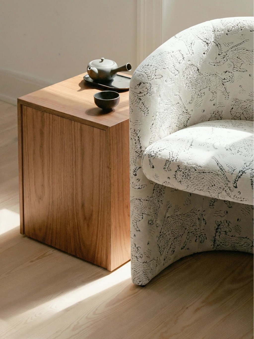 New Works Covent Club Chair, a luxurious upholstered chair in white fabric with abstract black patterns, shown next to a natural wood side table. Perfect for modern living spaces.