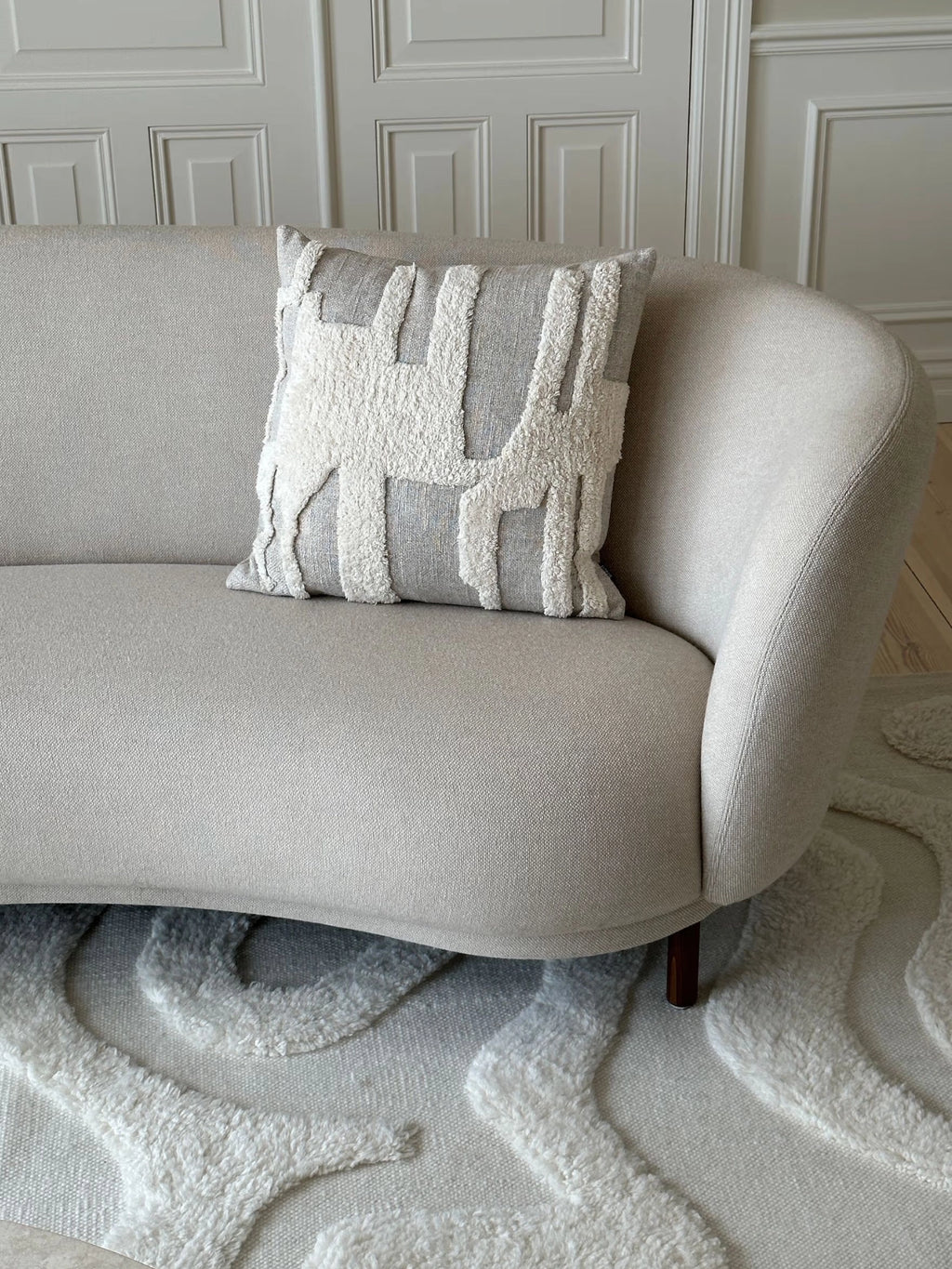 Tinted Objects Eksand Throw Pillow, a stylish square cushion featuring a textured cream-colored tufted abstract pattern against a light gray woven fabric base, resting on a beige modern sofa. This decorative accent pillow is perfect for adding contemporary comfort and visual interest to any living space or bedroom for stylish home decor enthusiasts.