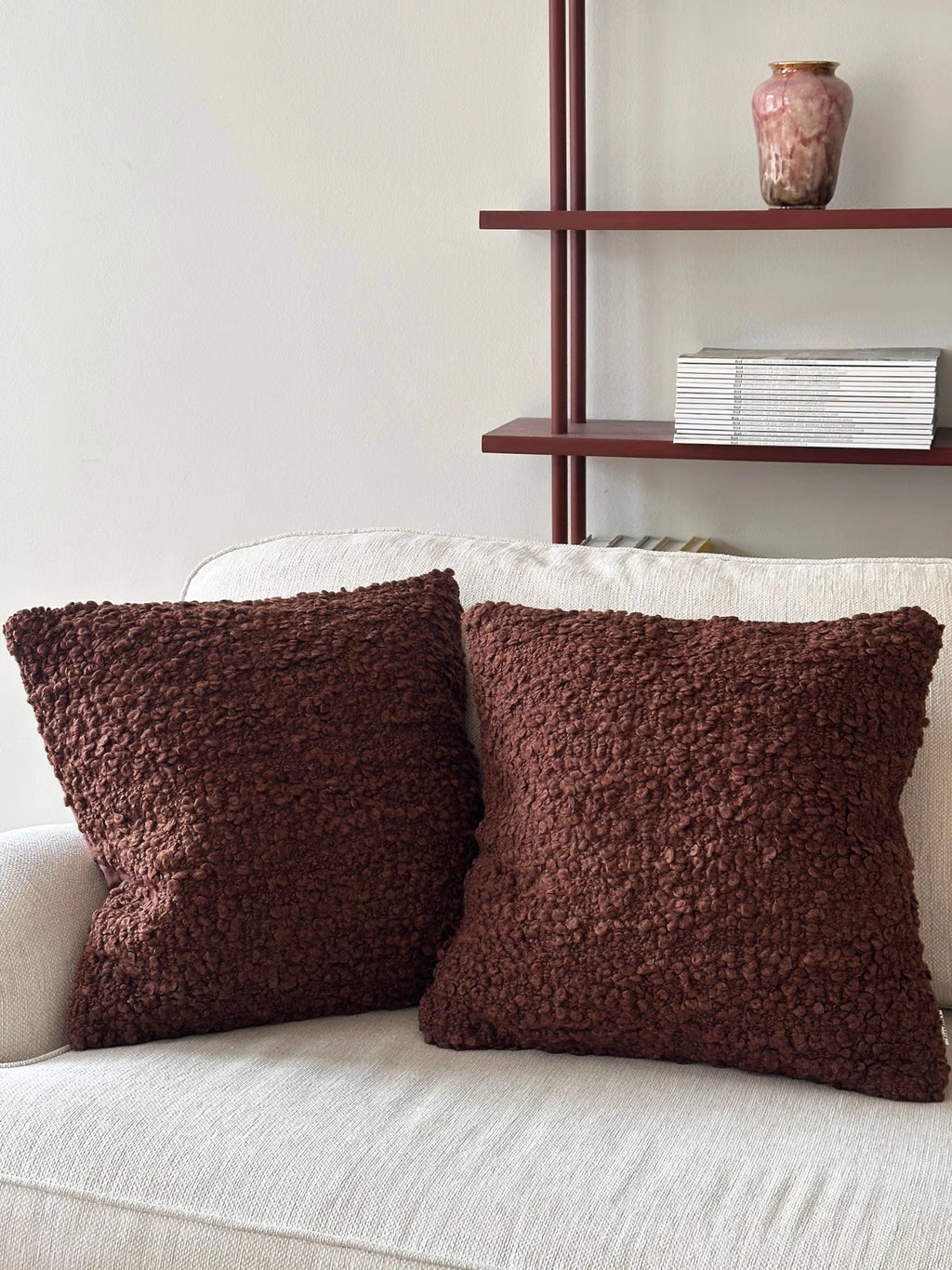 Tinted Objects Levantin Boucle Throw Pillow, two square brown boucle cushions with a rich, textured finish, styled on a neutral sofa. These stylish decorative throw pillows are perfect for adding luxurious comfort and warmth to any modern living space.