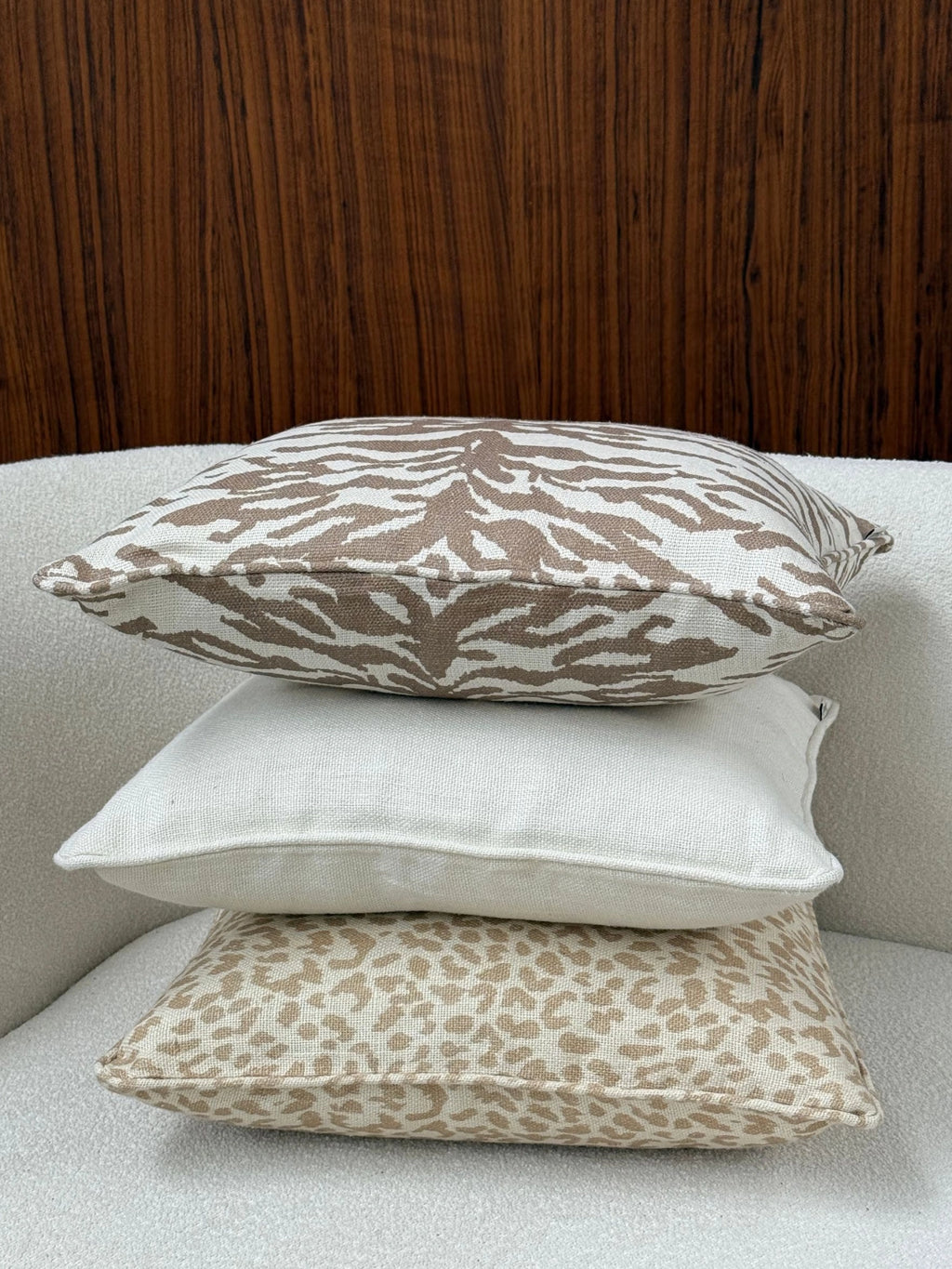 Tinted Objects Norell Throw Pillow, a stack of three decorative cushions featuring a top cushion with a brown zebra print, a middle plain cream cushion, and a bottom cushion with a beige leopard print, all in a textured fabric. These stylish accent pillows are perfect for adding comfort and a chic touch to any modern living space or bedroom.