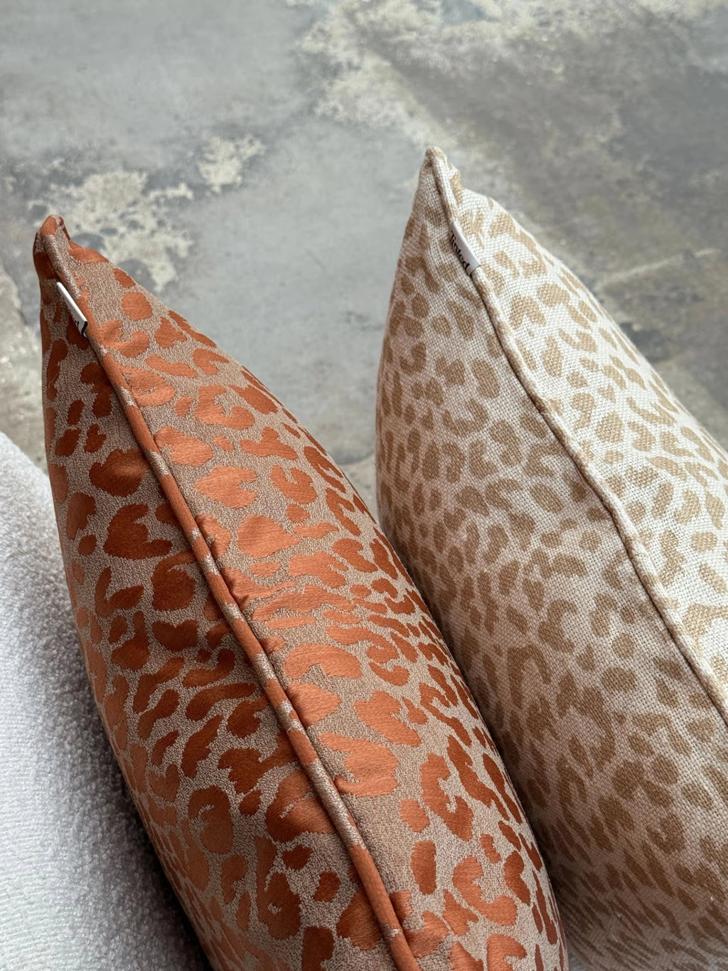Tinted Objects Vildklint Throw Pillow, featuring two stylish leopard print cushions: one in rich rust orange and beige, the other in light beige and tan, both with visible piping details and a soft textured fabric. These decorative cushions are perfect for adding a touch of modern comfort and wild elegance to any living room or bedroom decor.