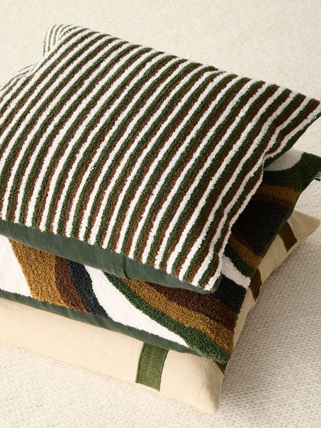 Chhatwal & Jonsson Raipur Boucle Throw Pillow, a stack of textured decorative cushions featuring a plush forest green, brown, and cream striped bouclé fabric pillow on top.