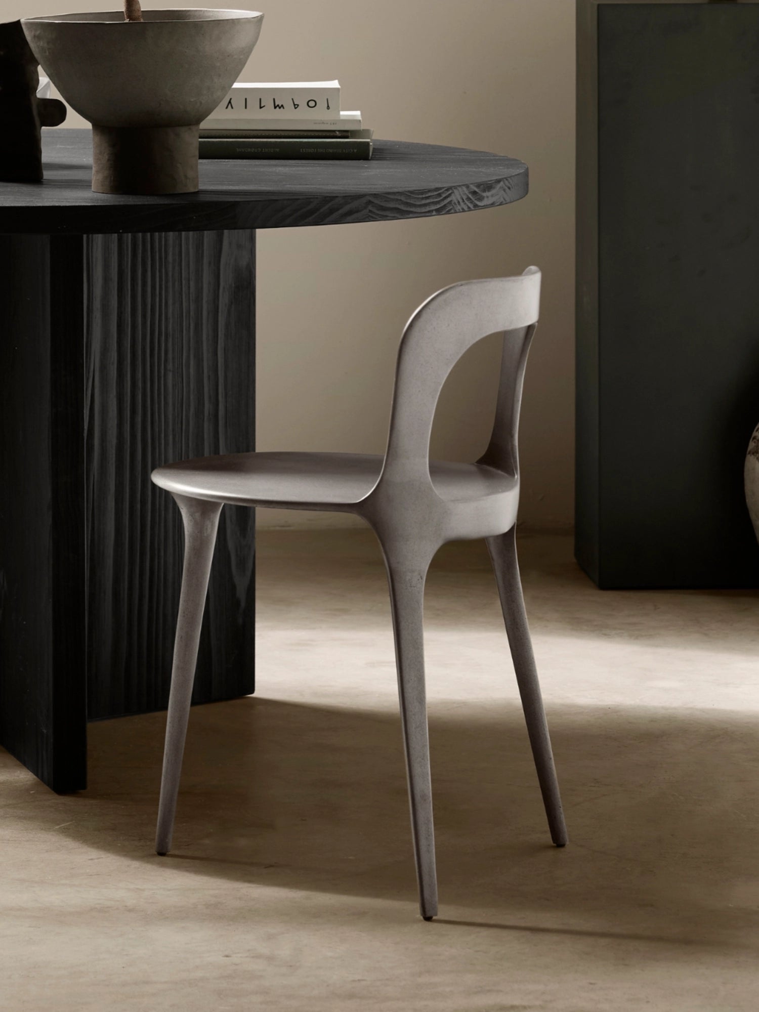 Tine K Dune Recycled Aluminium Chair, a dark grey sculptural dining chair crafted from recycled aluminum with a matte, slightly textured finish and fluid, organic modern design. It features a gently curved backrest with a distinctive cutout and slender, tapered legs. Ideal for contemporary dining rooms, minimalist interiors, or as a striking brutalist-inspired accent chair.