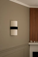Wall-mounted light fixture with a black band on a beige wall next to a fireplace.