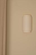 Beige wall sconce on a beige wall with a curtain to the left