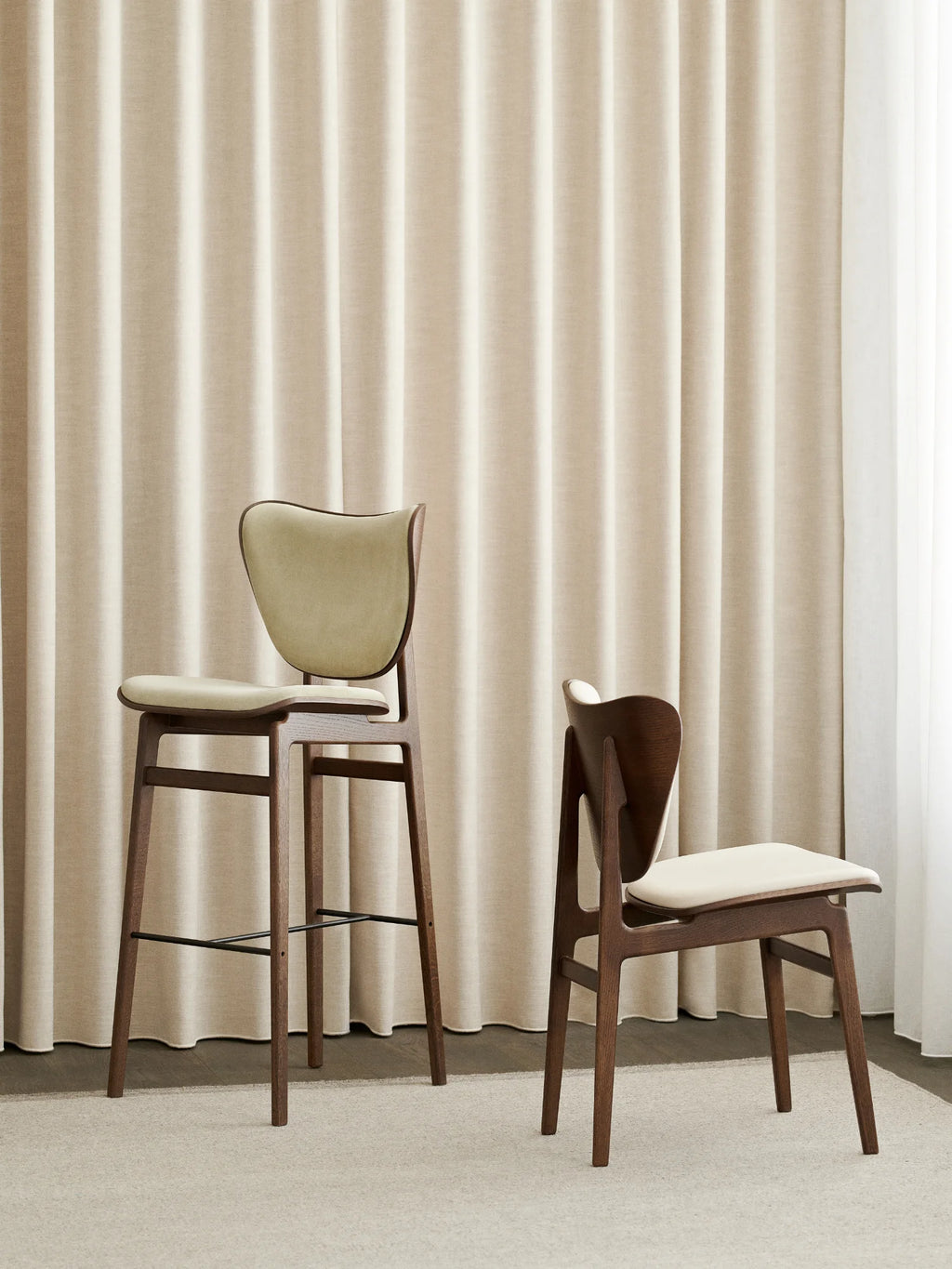 NORR11 Elephant Bar Chair and dining chair. Two elegant, dark stained oak chairs with cream upholstered seats, displayed in a modern interior. Ideal for sophisticated kitchen or dining areas.