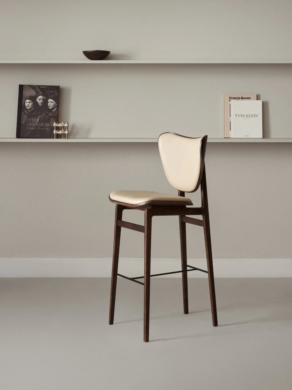 NORR11 Elephant Bar Chair, showcasing its curved off-white upholstered seat and backrest on a sophisticated dark walnut timber frame, in a lifestyle setting. This premium bar chair offers authentic Scandinavian design for modern interiors.