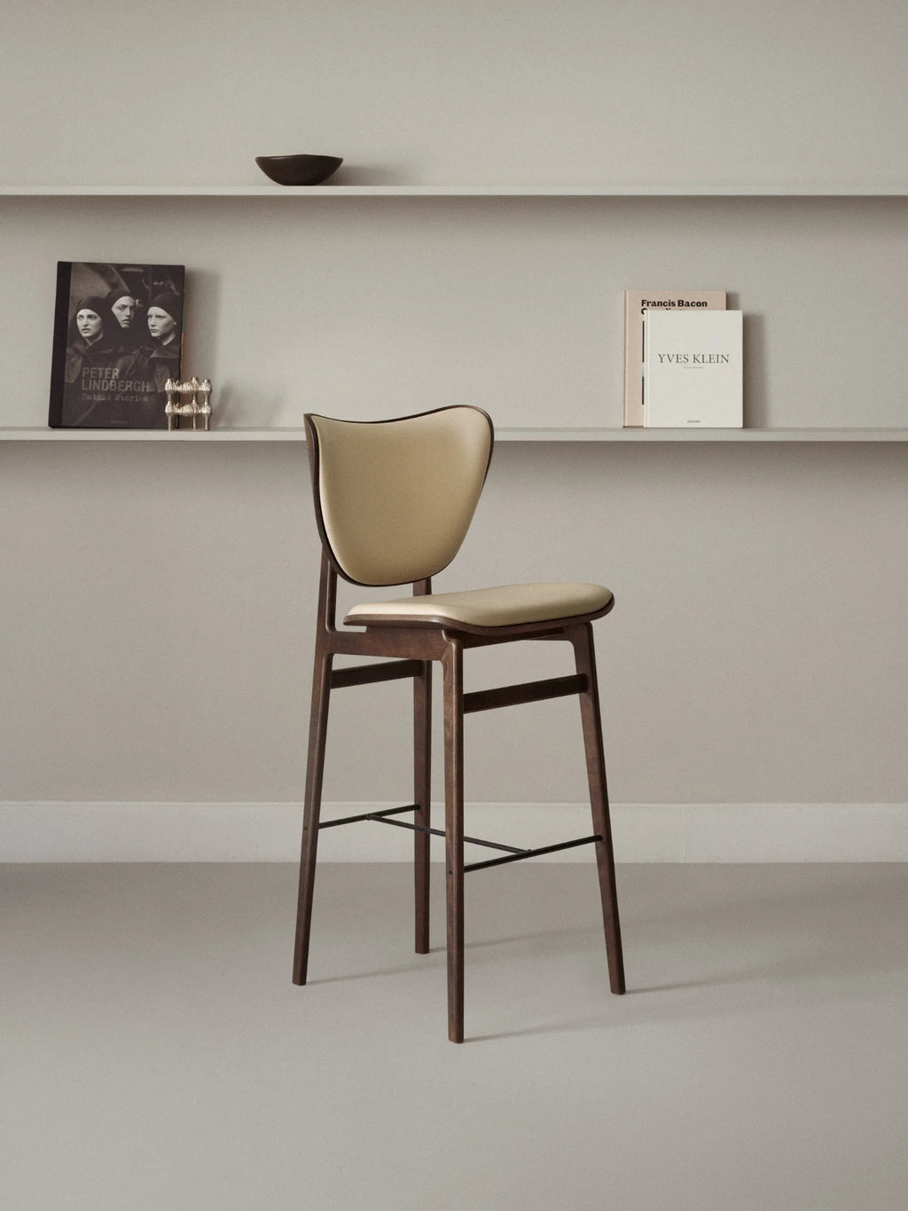 NORR11 Elephant Bar Chair, showcasing a dark brown stained oak wood frame, curved backrest, and padded cream leather cushions, displayed in a sophisticated interior setting. A premium, authentic bar stool design.