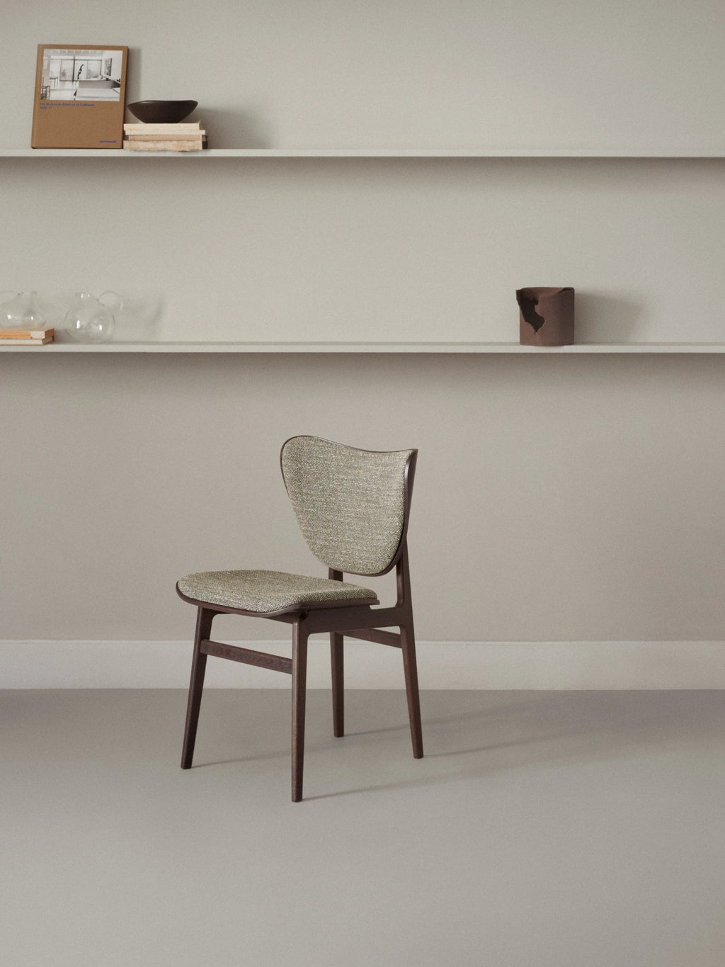 NORR11 Elephant Chair, a distinctive mid-century modern dining chair crafted from dark stained solid wood with elegantly tapered legs and a unique, organically curved backrest. It features comfortable light grey-beige woven fabric upholstery on both the seat and the back, providing a refined texture and inviting feel. Perfect as a stylish Scandinavian dining chair, contemporary kitchen chair, or sophisticated accent piece for a home office.