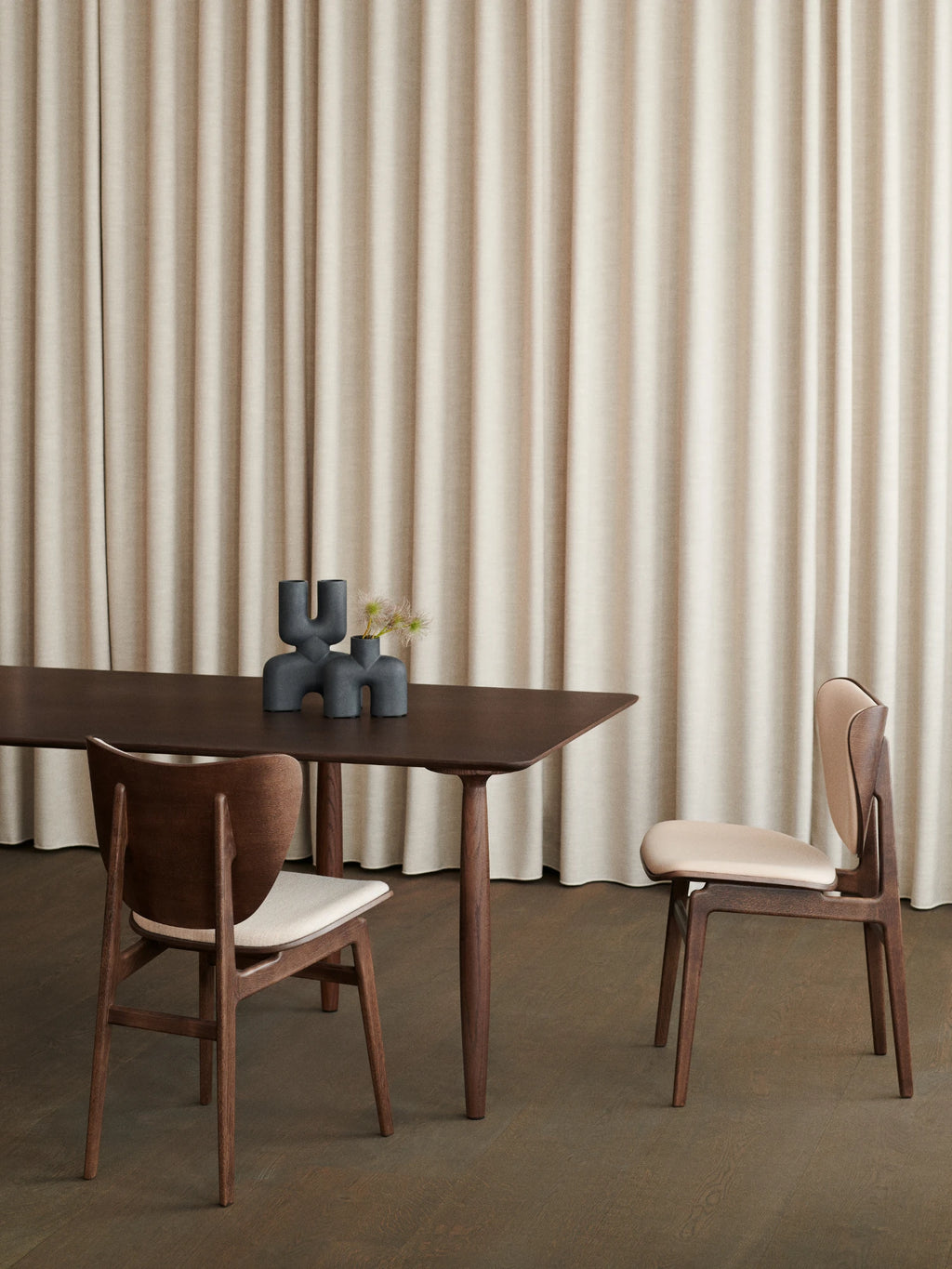 NORR11 Elephant Chair, a sleek Scandinavian dining chair crafted from dark solid wood with a gracefully curved backrest and slender, tapered legs. It features a comfortable light beige upholstered seat and matching back pad, offering a minimalist yet organic modern design. Perfect as a contemporary dining room chair or stylish accent for Nordic-inspired living spaces.