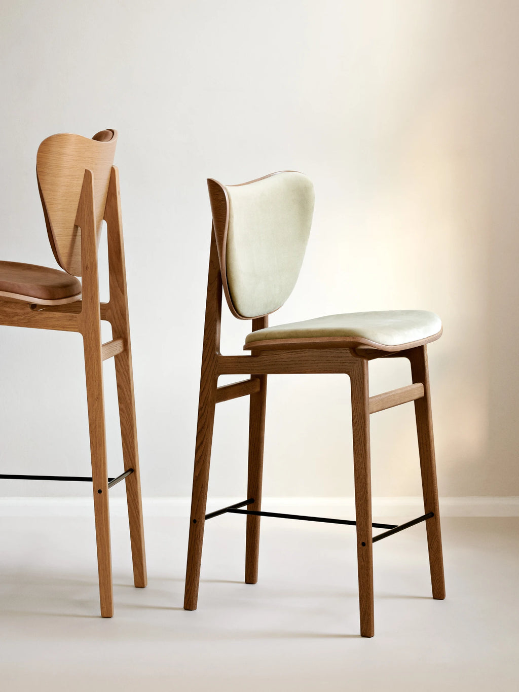 NORR11 Elephant Counter Chair, a Scandinavian solid oak bar stool featuring a distinctive curved 'elephant ear' backrest and ergonomic seat, upholstered in a soft light sage green fabric, complemented by elegant.