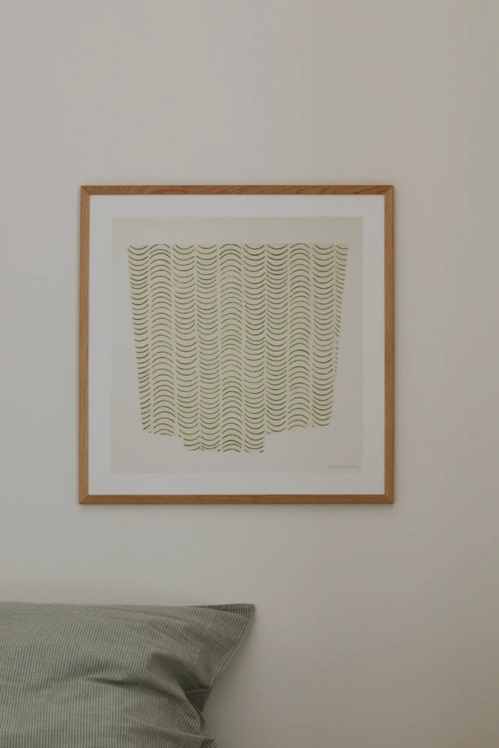The Poster Club Something to Keep, a minimalist abstract art print featuring a pattern of vertical dark green wavy lines on a warm beige background, framed in a light natural oak frame with a crisp white mat. This organic modern poster is ideal for Scandinavian bedrooms, contemporary living rooms, or adding a calm, neutral accent to a gallery wall.
