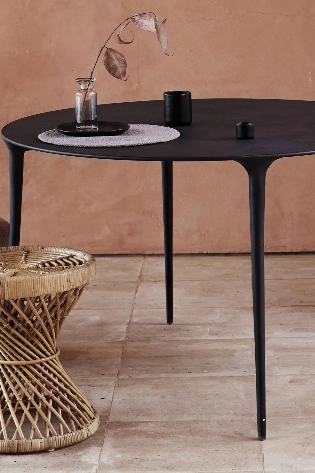 Tine K Feel Metal Round Dining Table, a modern minimalist dining table crafted from matte black metal with a smooth round tabletop and sleek tapered legs that create a contemporary silhouette. This versatile black dining table offers a refined aesthetic, ideal for modern dining rooms, stylish kitchens, or compact living spaces.