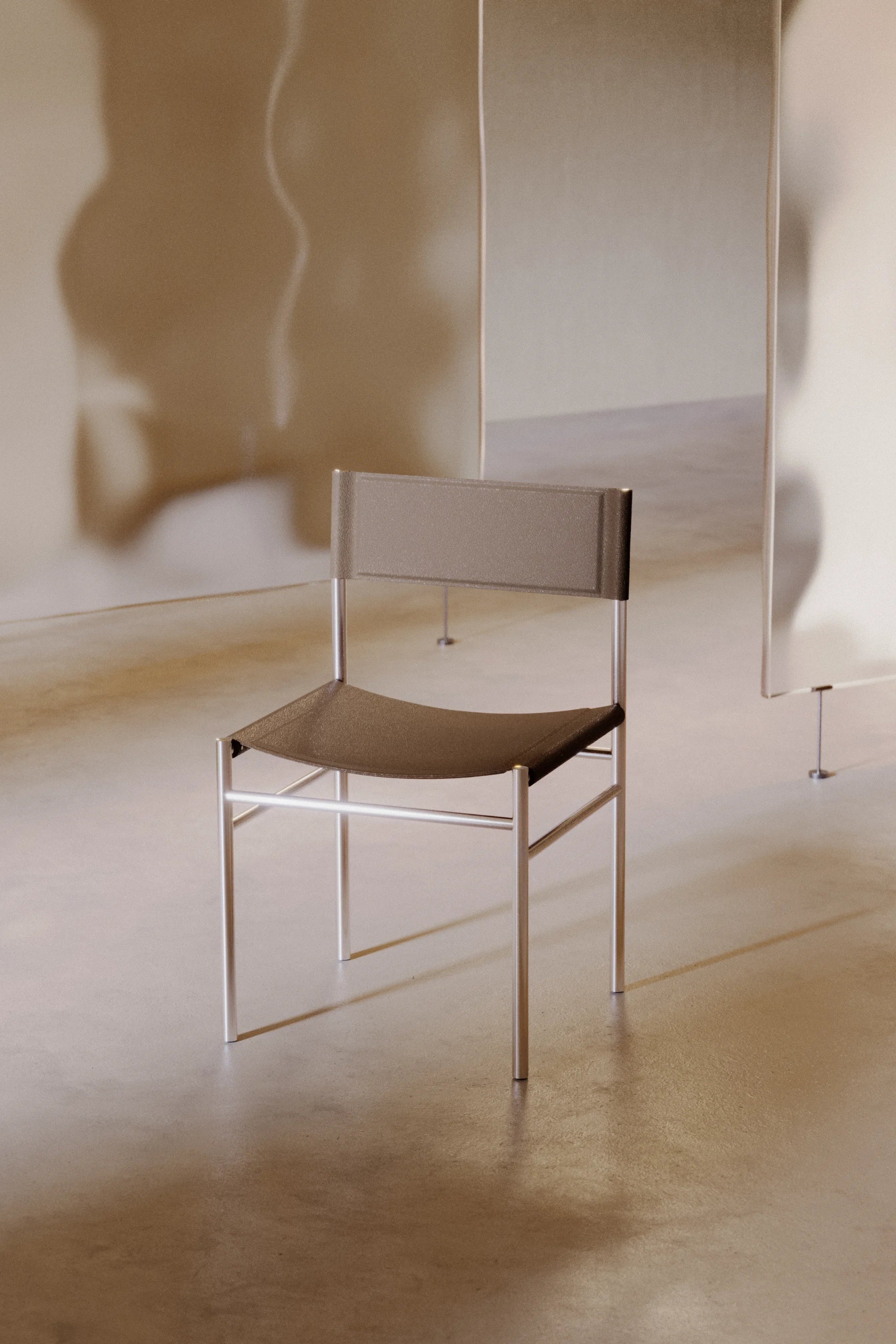 Minimalist chair with a metallic frame and brown seat in a neutral setting