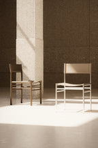 Two chairs in a minimalistic setting with a textured wall and light source.