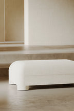 White ottoman on a wooden floor with a neutral wall background