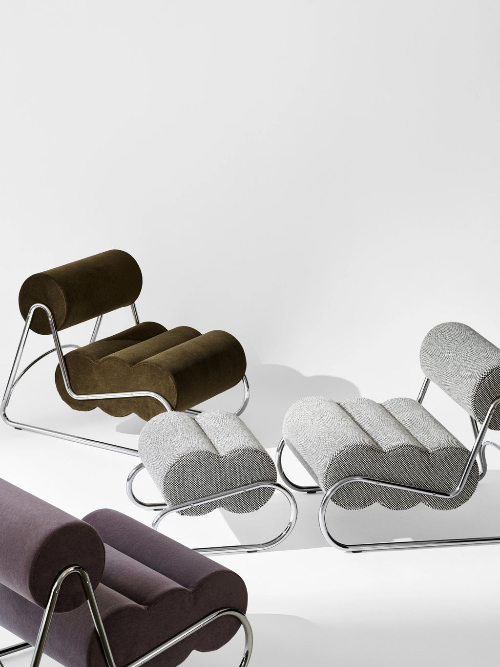NORR11 Fave Footstool, a brutalist contemporary footstool featuring a distinctive wavy, tubular design upholstered in luxurious dark olive green velvet, light grey speckled fabric, and dark plum velvet.