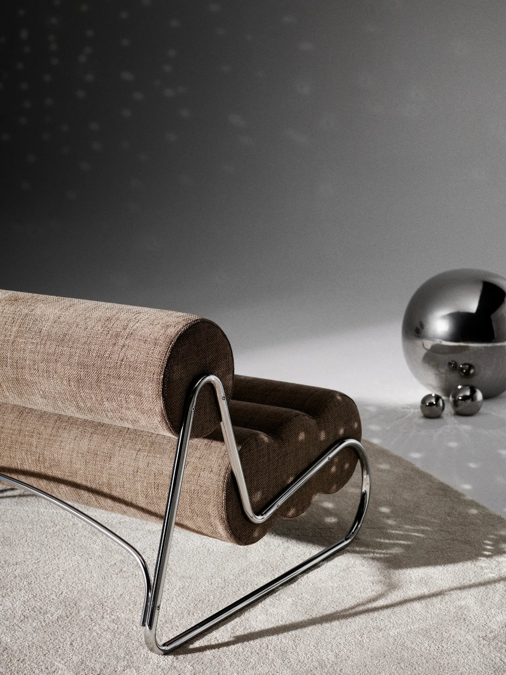 NORR11 Fave Sofa, a modern sculptural sofa featuring plush cylindrical cushions upholstered in a textured beige woven fabric with contrasting dark brown ends, supported by a sleek polished chrome tubular steel frame. This compact, minimalist design offers a contemporary lounge experience, perfect for stylish living rooms, apartment spaces, or design-forward reception areas.