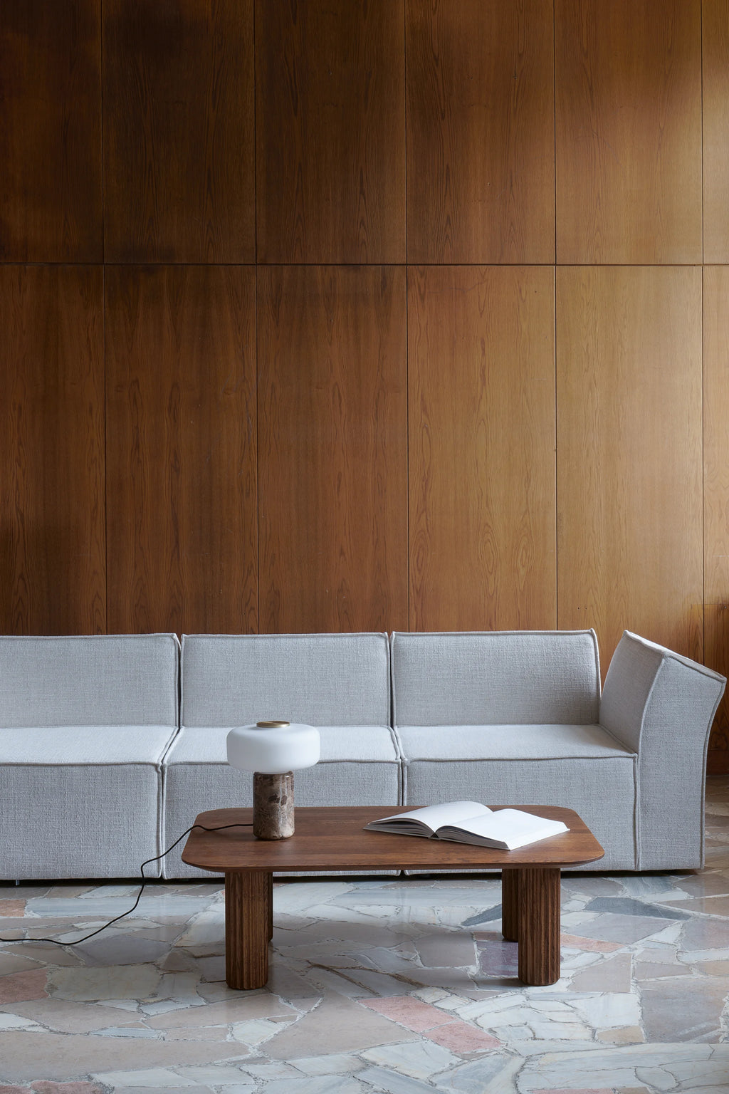 TAMO Filar Coffee Table, a luxury richly grained dark brown wood table with rounded corners and fluted cylindrical legs, styled with a modern lamp and book. Perfect for a refined living space.