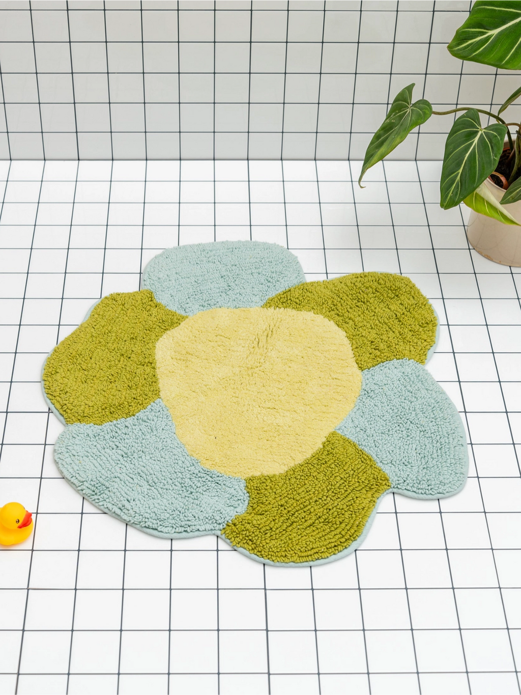 TARTA GELATINA Gardenia Bath Mat, a playful floral bath mat crafted from plush tufted cotton, featuring an organic flower shape with rounded petals in a vibrant color palette of soft pastel yellow, olive green, and light blue. This whimsical shaggy bath mat is perfect for adding a retro-inspired touch to a modern bathroom, kids' room, or playful nursery decor.
