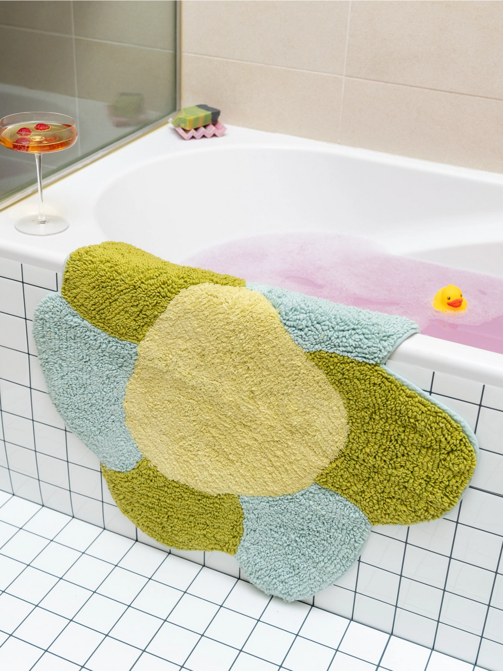 TARTA GELATINA Gardenia Bath Mat, a plush organic modern bath mat crafted from soft tufted cotton, featuring an abstract, irregular shape composed of vibrant chartreuse green, pale yellow, and light blue sections. This colorful, shaggy bathroom rug adds a playful and contemporary accent, perfect for modern bathroom decor and unique interior styling.