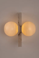 Wall-mounted light fixture with two round glass shades on a neutral background