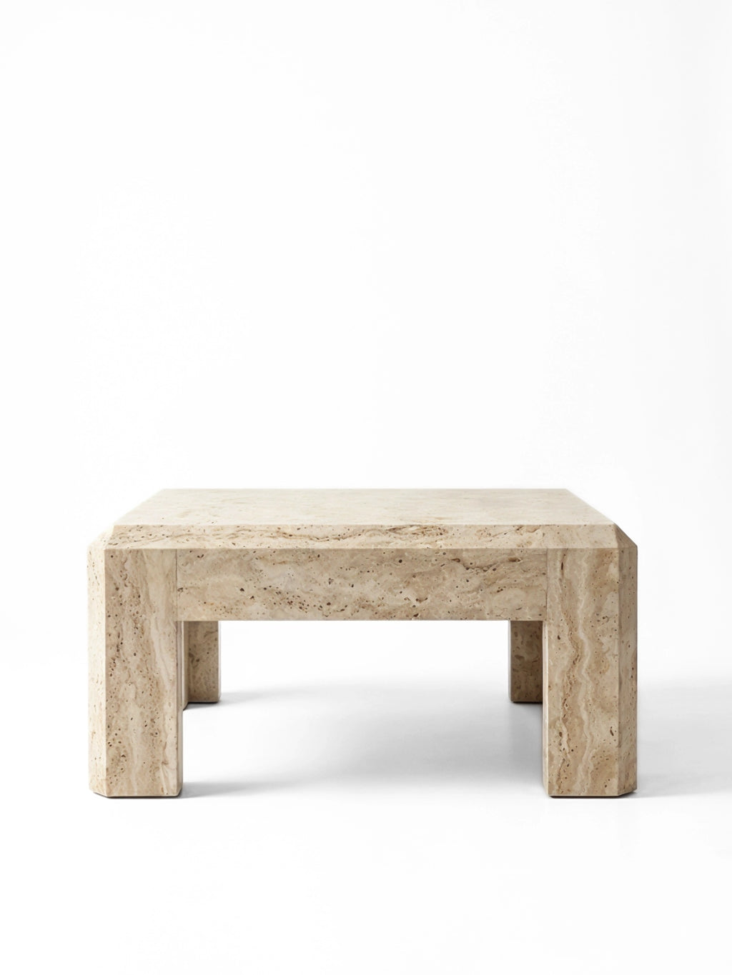 TCL Studios Form Coffee Table, a chunky brutalist coffee table crafted entirely from natural beige travertine stone with a porous texture and warm neutral tones. Its rectangular silhouette features thick block legs and distinctive chamfered edges, embodying a minimalist yet robust design. Perfect as a statement piece in contemporary living rooms or organic modern lounge areas.