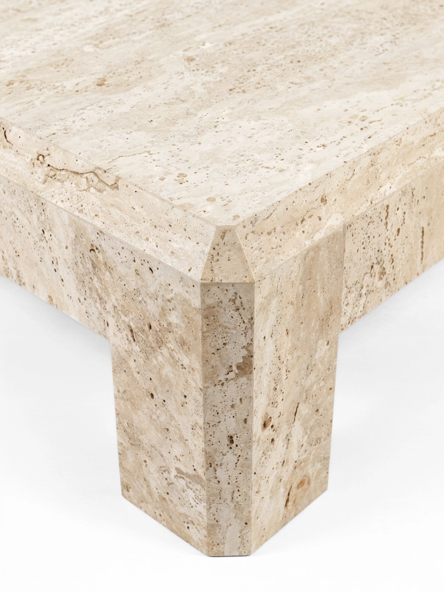 TCL Studios Form Coffee Table, a rectangular organic modern coffee table crafted from natural beige travertine stone, featuring a porous texture with subtle veining and warm cream tones. This minimalist coffee table showcases a sturdy block silhouette with uniquely angled edges where the top meets the legs, reflecting a brutalist aesthetic.