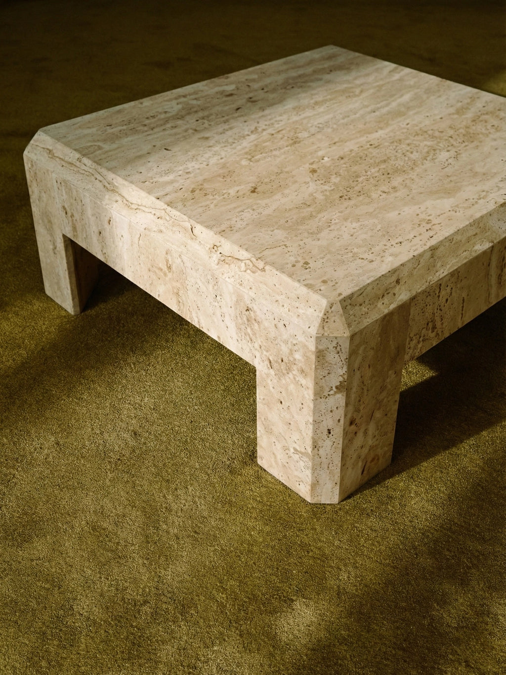 TCL Studios Form Coffee Table, a chunky brutalist coffee table crafted from natural beige travertine stone with a distinctive porous texture and warm, creamy tones. Its sculptural, minimalist design features a thick square top and block legs with faceted edges, creating a bold statement piece. Perfect as a contemporary living room centerpiece or for organic modern and minimalist interiors.