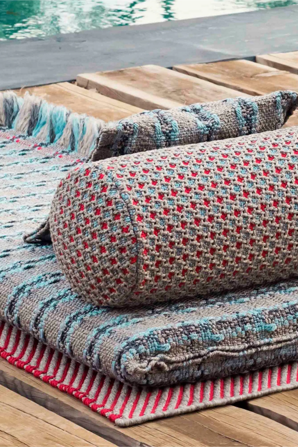 GAN Rugs Garden Layers Composition 06, a vibrant outdoor sofa collection featuring textured grey hand-woven cushions and a matching rug with red, blue, and teal accents.