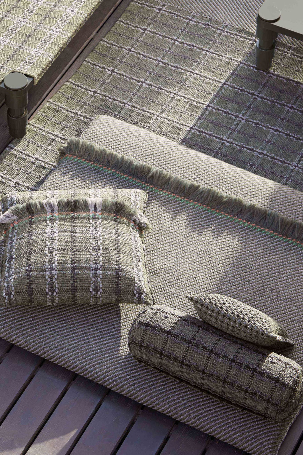 GAN Rugs Garden Layers Composition 03, an organic modern outdoor sofa lounge set featuring a large olive green woven outdoor mattress with a subtle striped texture and fringed edges, accented with thin orange and light.