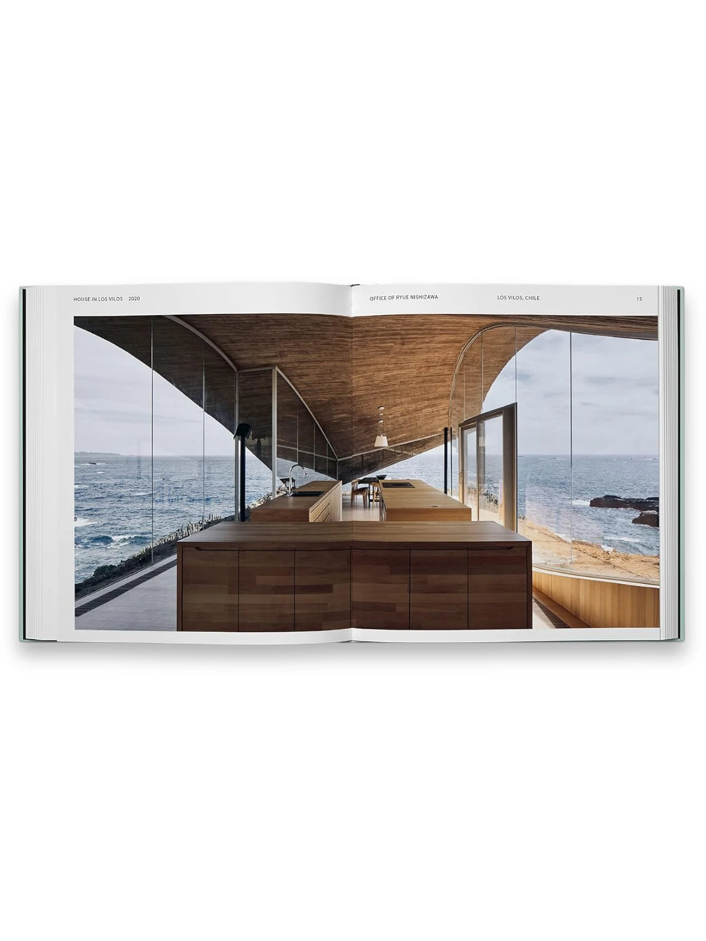 Book Glass Houses, an open architecture book displaying a modern kitchen with rich wooden cabinetry and a curved concrete ceiling, featuring floor-to-ceiling windows overlooking a dramatic ocean landscape. This visually stunning architecture book is perfect for design enthusiasts and professionals seeking inspiration from innovative residential designs.