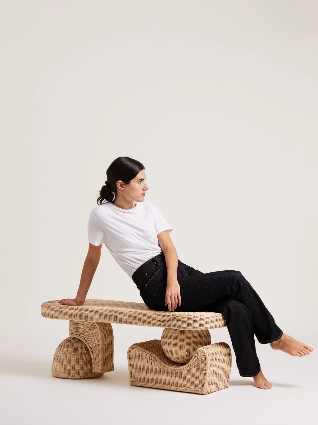 Heaps & Woods Alfred Bench, a unique sculptural bench crafted from natural hand-woven rattan with an organic modern design. Its distinctive curved, architectural legs and light brown woven texture create a minimalist yet inviting aesthetic. Perfect as an entryway bench, living room accent, or bedroom seating for contemporary and organic-inspired spaces.
