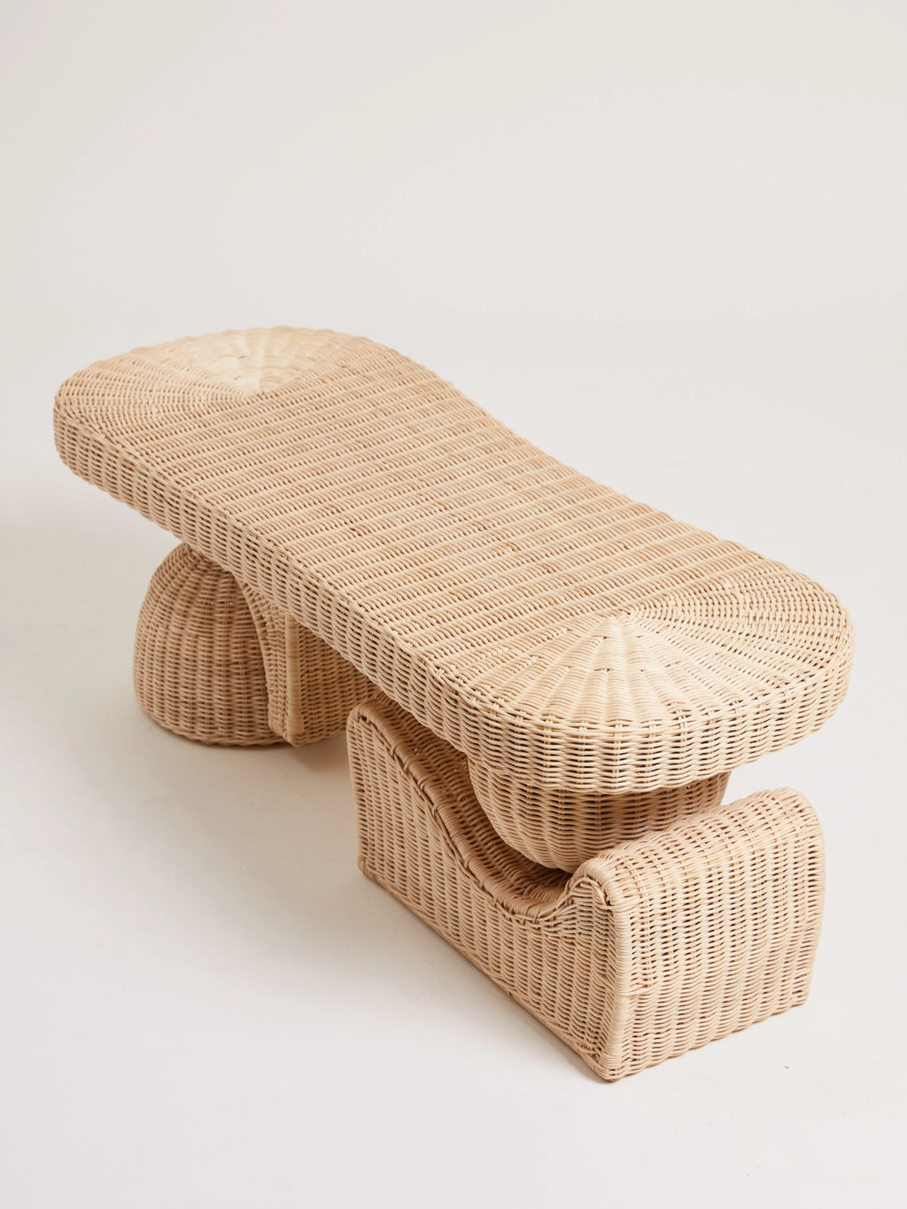 Heaps & Woods Alfred Bench, a sculptural organic modern bench crafted from natural woven rattan in a light beige finish, featuring an elongated rectangular top and two distinct rounded, arched bases. This versatile rattan bench is ideal for a coastal entryway, boho living room, or contemporary bedroom accent.