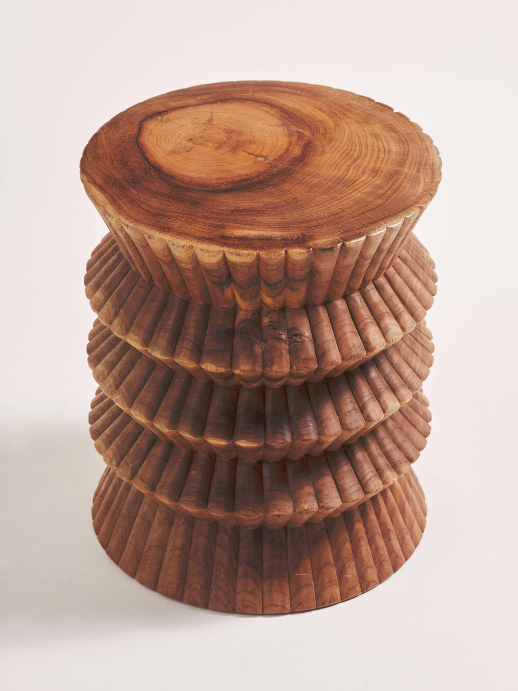 Heaps & Woods Carla Stool, a warm brown solid wood stool featuring a beautifully carved, tiered, and fluted cylindrical body with a smooth, natural wood slice top showcasing visible grain and rings. This handcrafted wood accent table offers an organic modern or rustic aesthetic, perfect as a side table for living rooms, a bedroom accent, or unique entryway decor in contemporary spaces.