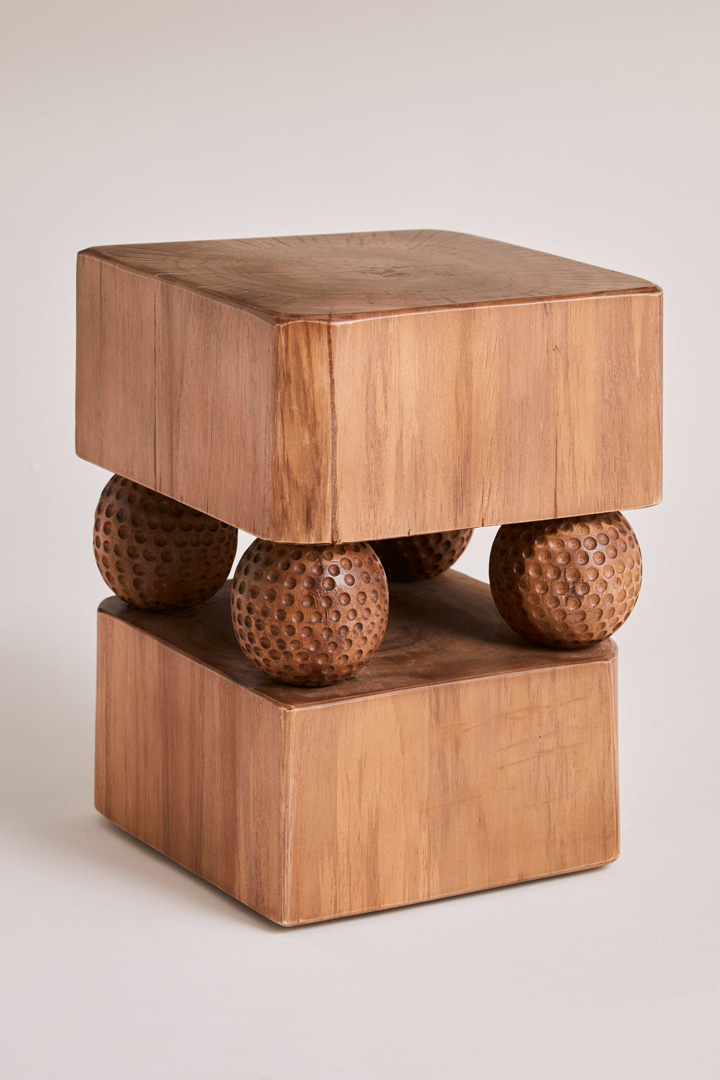 Heaps & Woods Gabi Stool, a sculptural solid wood accent table featuring two thick square blocks of natural warm-toned wood, separated by four uniquely dimpled, spherical wooden legs. This brutalist-inspired or organic modern stool showcases a rich wood grain and intriguing texture. Ideal as a rustic side table in a living room, a unique bedside table, or contemporary accent furniture.