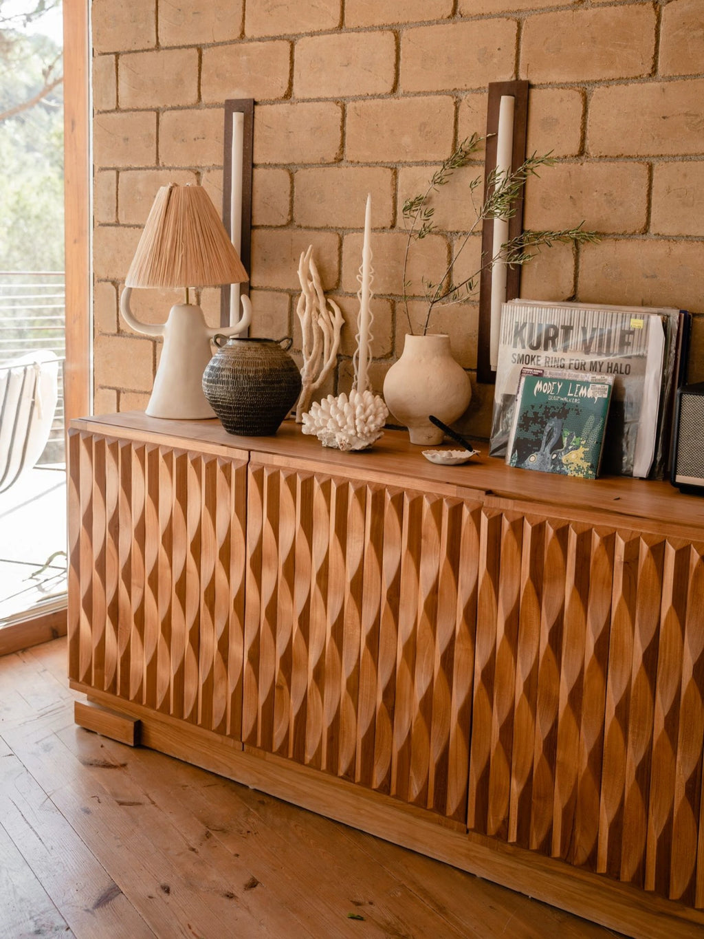 Heaps & Woods Luisa Console, an organic modern solid wood console table featuring four doors with a deeply carved, rhythmic wave pattern in a warm natural wood finish. This contemporary sideboard offers sculptural texture and ample storage for the living room or dining room. Ideal as a statement piece for a sophisticated entryway, modern minimalist, or organic brutalist interior.
