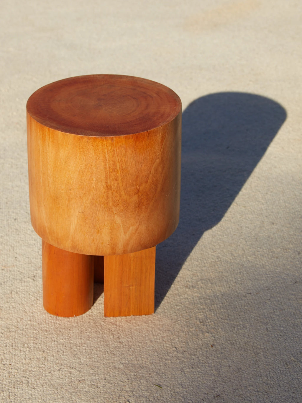 Heaps & Woods Vaks Stool, a chunky solid wood stool crafted from warm reddish-brown wood, featuring a smooth cylindrical top with natural wood grain. Its unique sculptural base combines one round cylindrical leg with two flat rectangular legs, creating a robust, organic modern design. Ideal as a versatile side table, minimalist bedside table, or contemporary accent in living rooms and entryways.