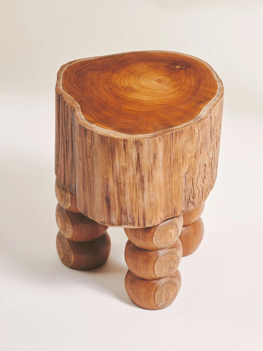 Heaps & Woods Vic Stool, a rustic organic modern stool crafted from solid natural wood, featuring a live edge tree stump top with visible wood grain and a textured, bark-like cylindrical body. It stands on three unique carved bobble legs, showcasing a warm, rich brown finish. Ideal as a unique side table, accent stool, or plant stand for bohemian and natural-inspired living rooms or bedrooms.