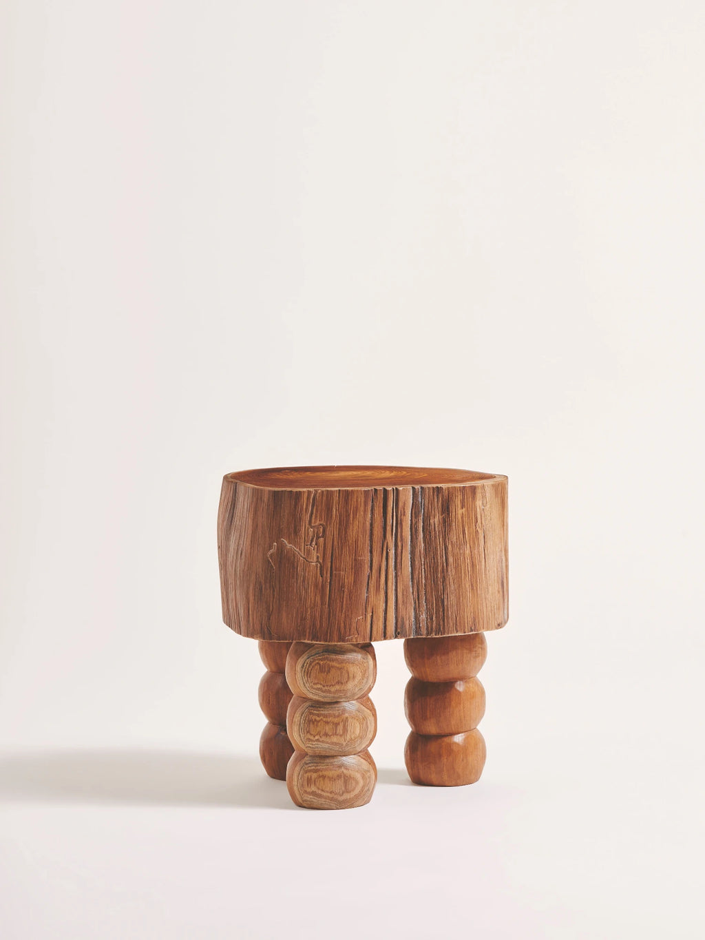 Heaps & Woods Vic Stool, a distinctive organic modern stool featuring a thick, natural wood slice top with visible grain and rustic edges. It is supported by three chunky, turned solid wood legs with a stacked spool design in warm natural wood tones. This handcrafted wood stool is perfect as a unique accent table, bedside table, or for adding organic texture to brutalist, rustic, or wabi-sabi living room or bedroom interiors.
