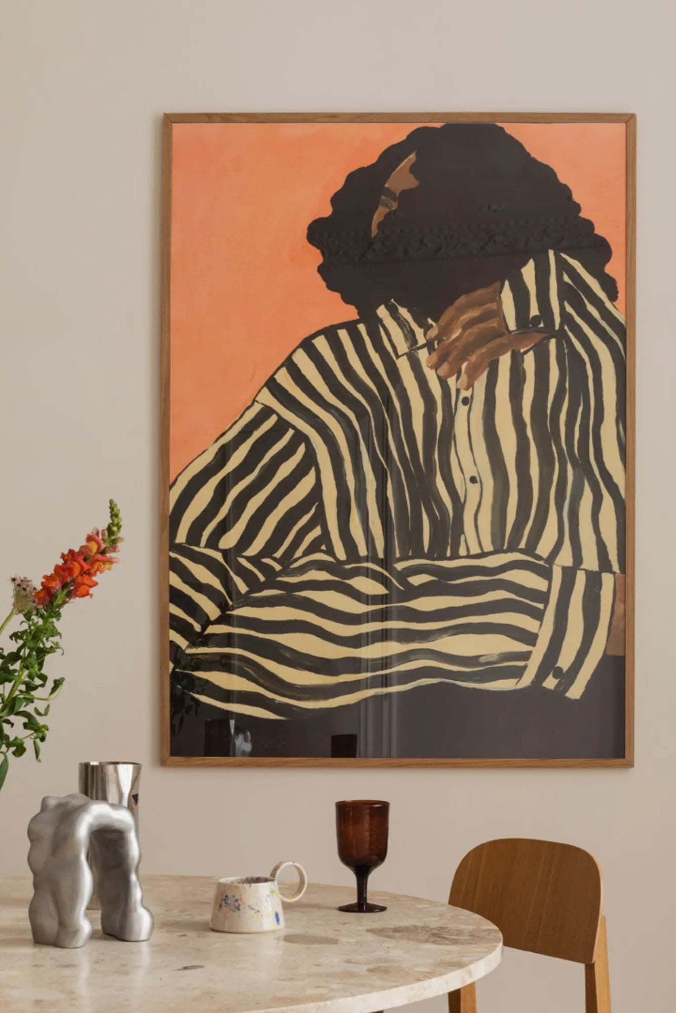 The Poster Club Serene Stripes, a captivating contemporary abstract figurative art print depicting a person wearing a bold black and cream striped shirt against a warm peach-orange background. The artwork features textured details in the dark, curly hair and is elegantly presented in a light natural oak frame. This modern wall art is ideal for adding a graphic and organic touch to Scandinavian living rooms, contemporary bedrooms, or curated gallery walls.