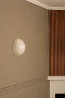 Round wall light fixture on a beige wall with wooden paneling.